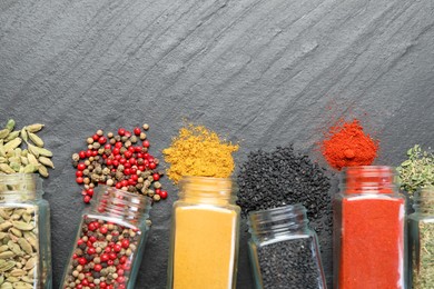Photo of Different aromatic spices in jars on black table, flat lay. Space for text