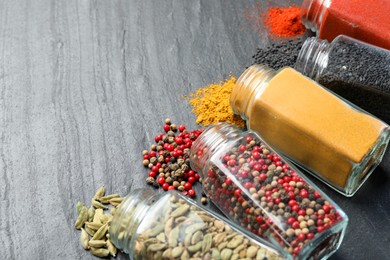 Photo of Different aromatic spices in jars on black table, closeup. Space for text