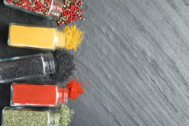 Photo of Different aromatic spices in jars on black table, flat lay. Space for text