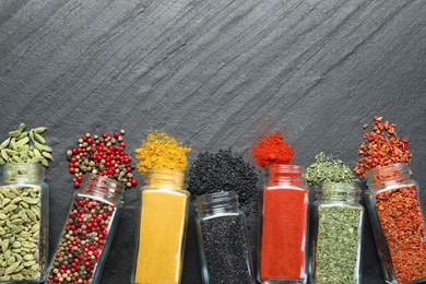 Photo of Different aromatic spices in jars on black table, flat lay. Space for text