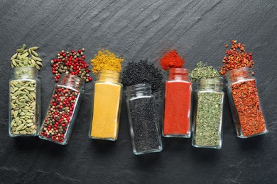 Photo of Different aromatic spices in jars on black table, flat lay