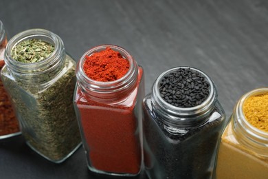 Photo of Different aromatic spices in jars on black table, closeup