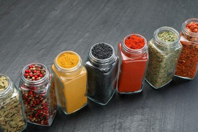 Photo of Different aromatic spices in jars on black table, closeup