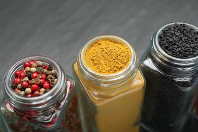 Photo of Different aromatic spices in jars on black table, closeup