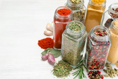 Photo of Different aromatic spices in jars on white table, closeup. Space for text