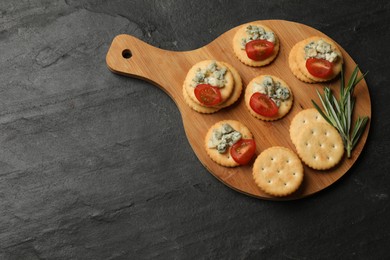 Photo of Tasty crackers with blue cheese, rosemary and tomatoes on dark textured table, top view. Space for text