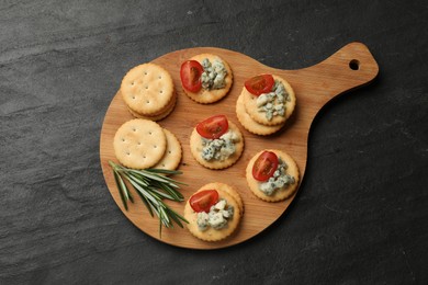 Photo of Tasty crackers with blue cheese, rosemary and tomatoes on dark textured table, top view