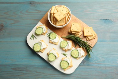 Photo of Tasty crackers with cream cheese, rosemary and cucumber on light blue wooden table, top view