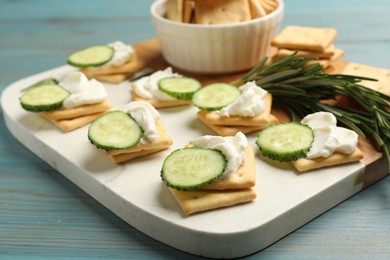 Photo of Tasty crackers with cream cheese, rosemary and cucumber on light blue wooden table, closeup