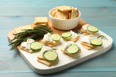 Photo of Tasty crackers with cream cheese, rosemary and cucumber on light blue wooden table, closeup