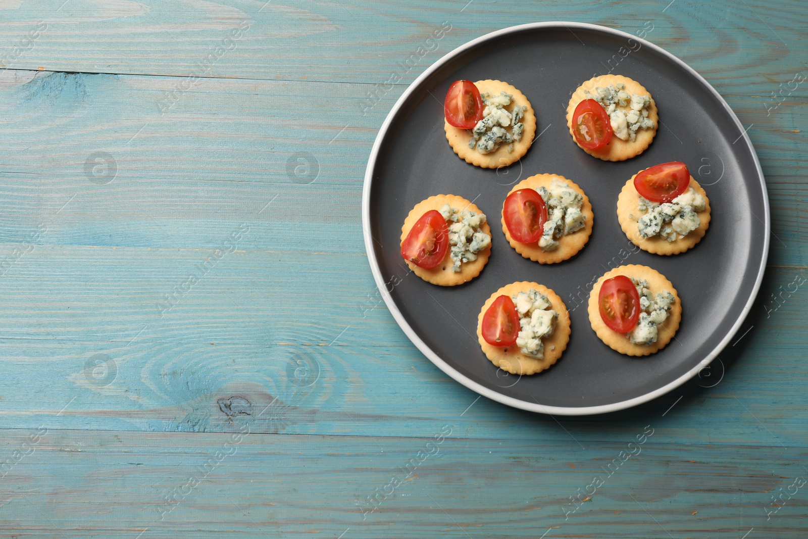 Photo of Tasty crackers with blue cheese and tomatoes on wooden table, top view. Space for text