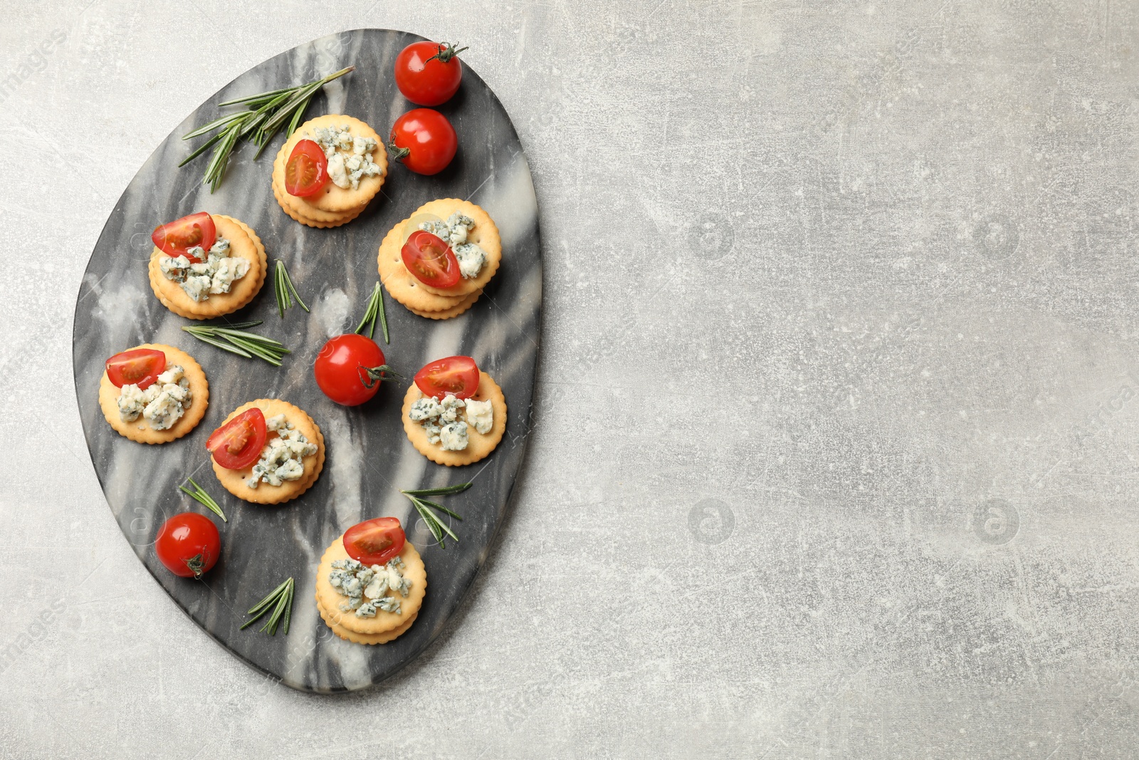 Photo of Tasty crackers with blue cheese, rosemary and tomatoes on grey textured table, top view. Space for text