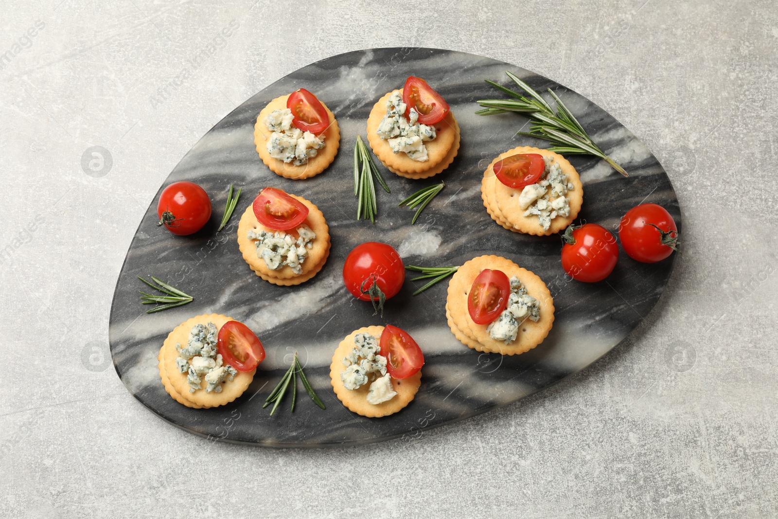 Tasty crackers with blue cheese, rosemary and tomatoes on grey textured table, top view Photo of Tasty crackers with blue cheese, rosemary and tomatoes on grey textured table, top view