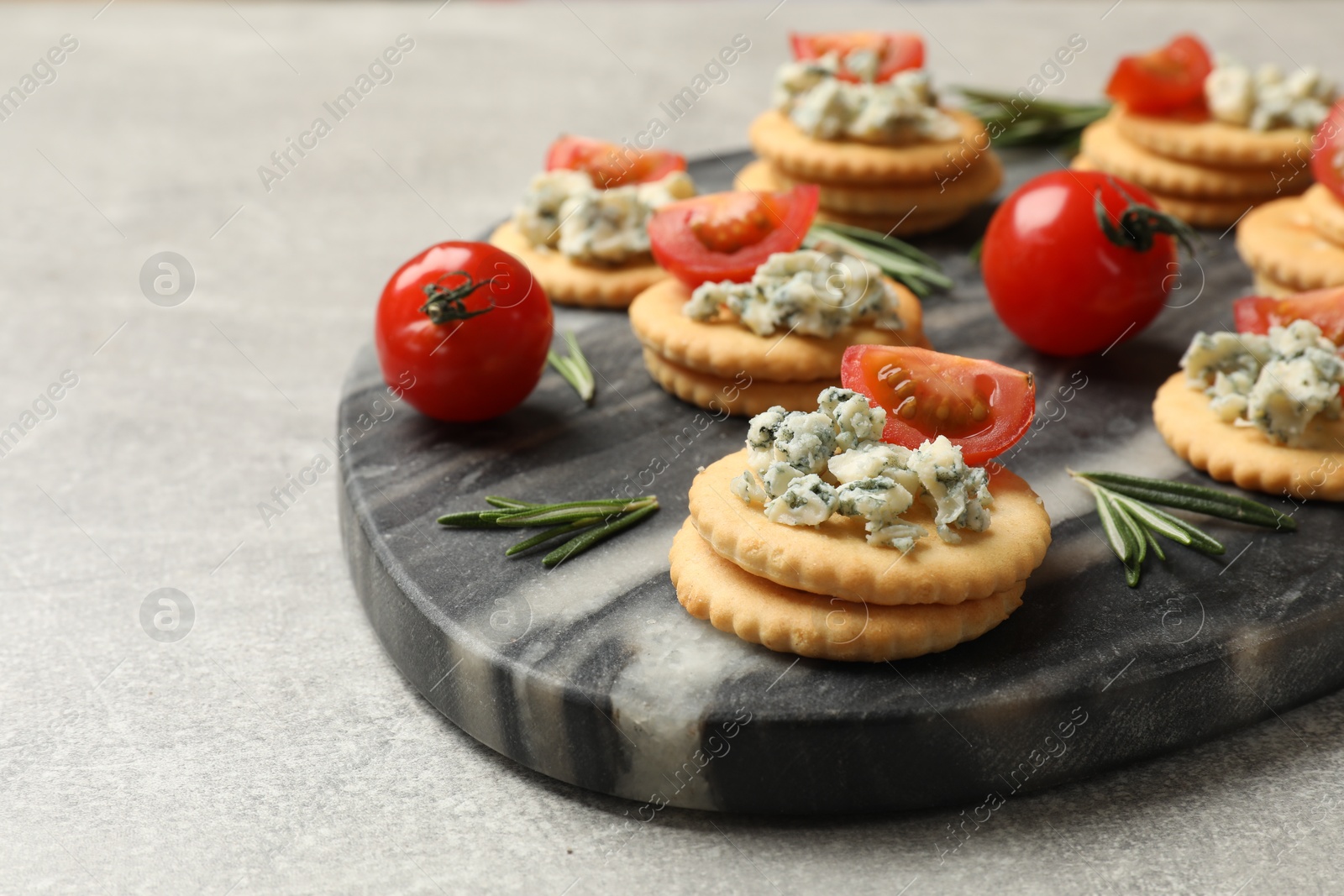 Photo of Tasty crackers with blue cheese, rosemary and tomatoes on grey textured table, closeup