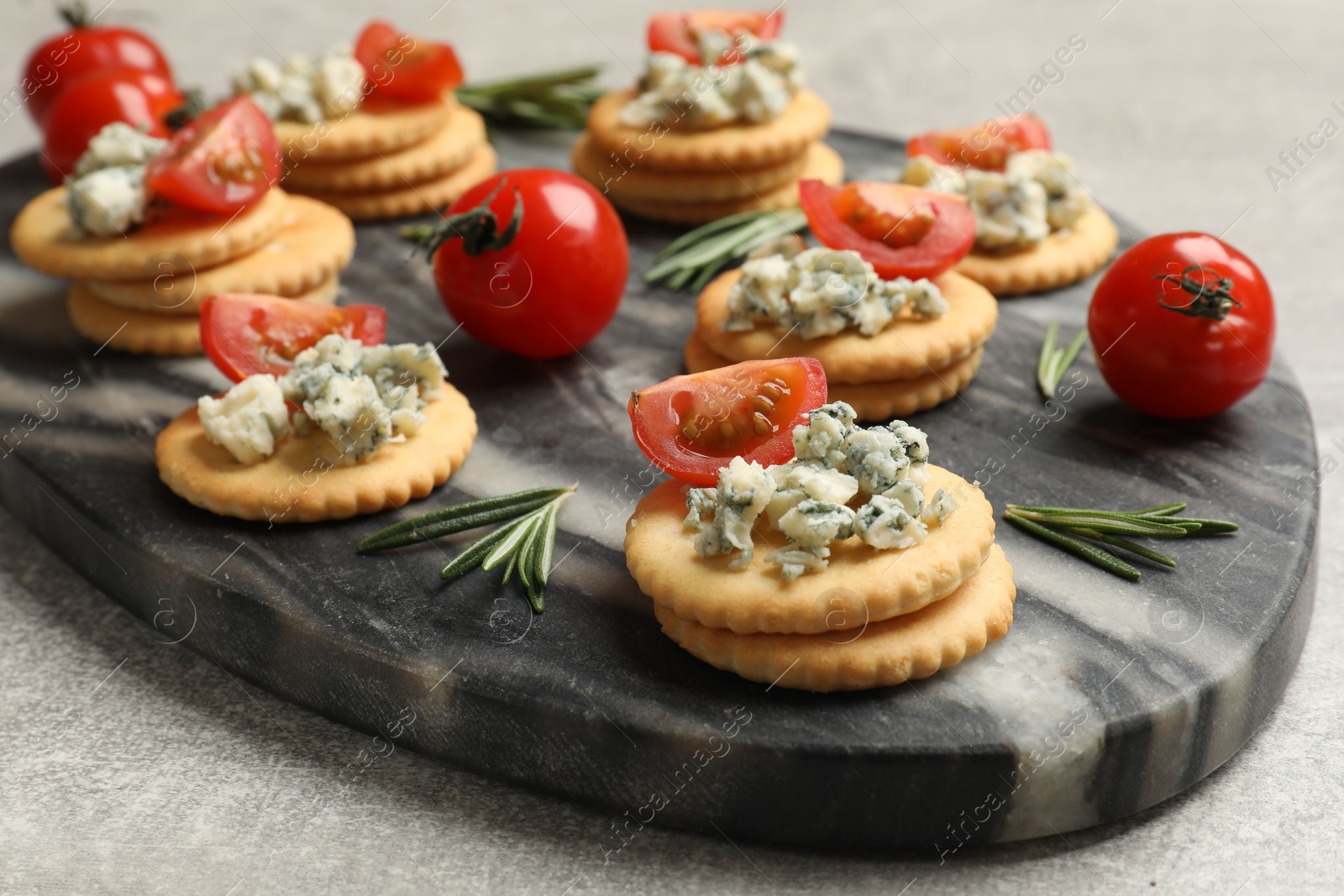 Tasty crackers with blue cheese, rosemary and tomatoes on grey textured table, closeup Photo of Tasty crackers with blue cheese, rosemary and tomatoes on grey textured table, closeup