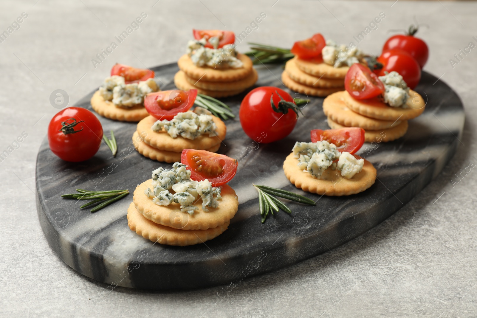 Tasty crackers with blue cheese, rosemary and tomatoes on grey textured table, closeup Photo of Tasty crackers with blue cheese, rosemary and tomatoes on grey textured table, closeup