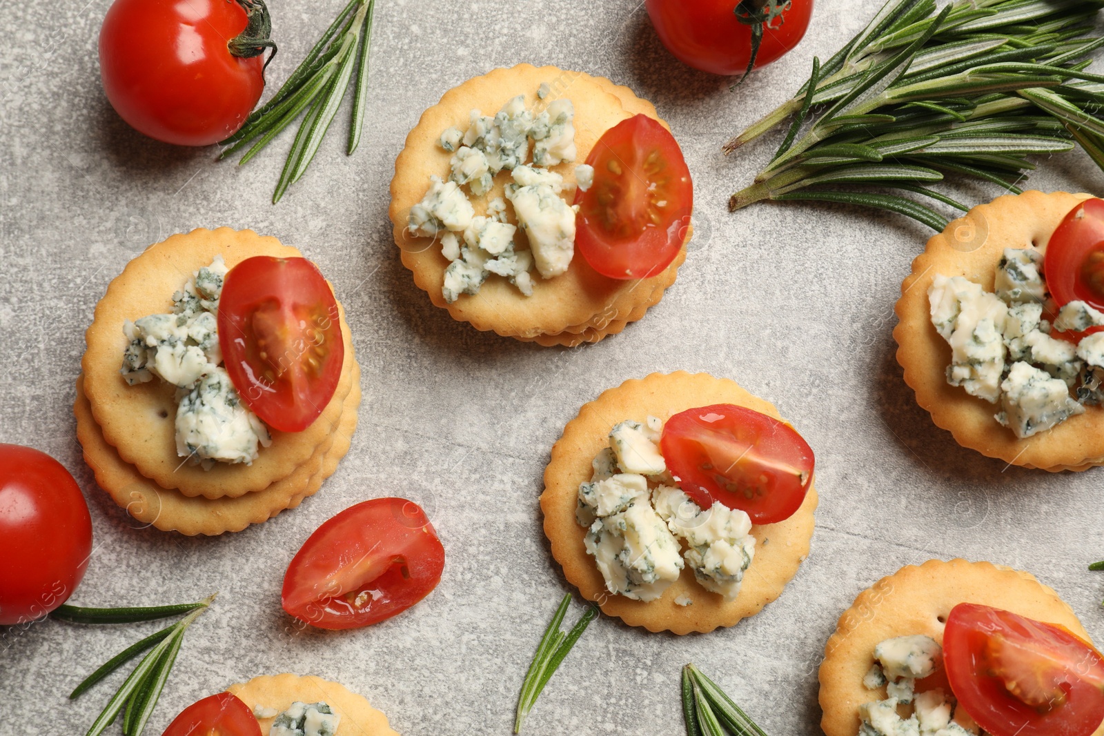 Tasty crackers with blue cheese, rosemary and tomatoes on grey textured table, flat lay Photo of Tasty crackers with blue cheese, rosemary and tomatoes on grey textured table, flat lay