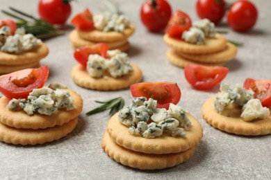 Photo of Tasty crackers with blue cheese, rosemary and tomatoes on grey textured table, closeup
