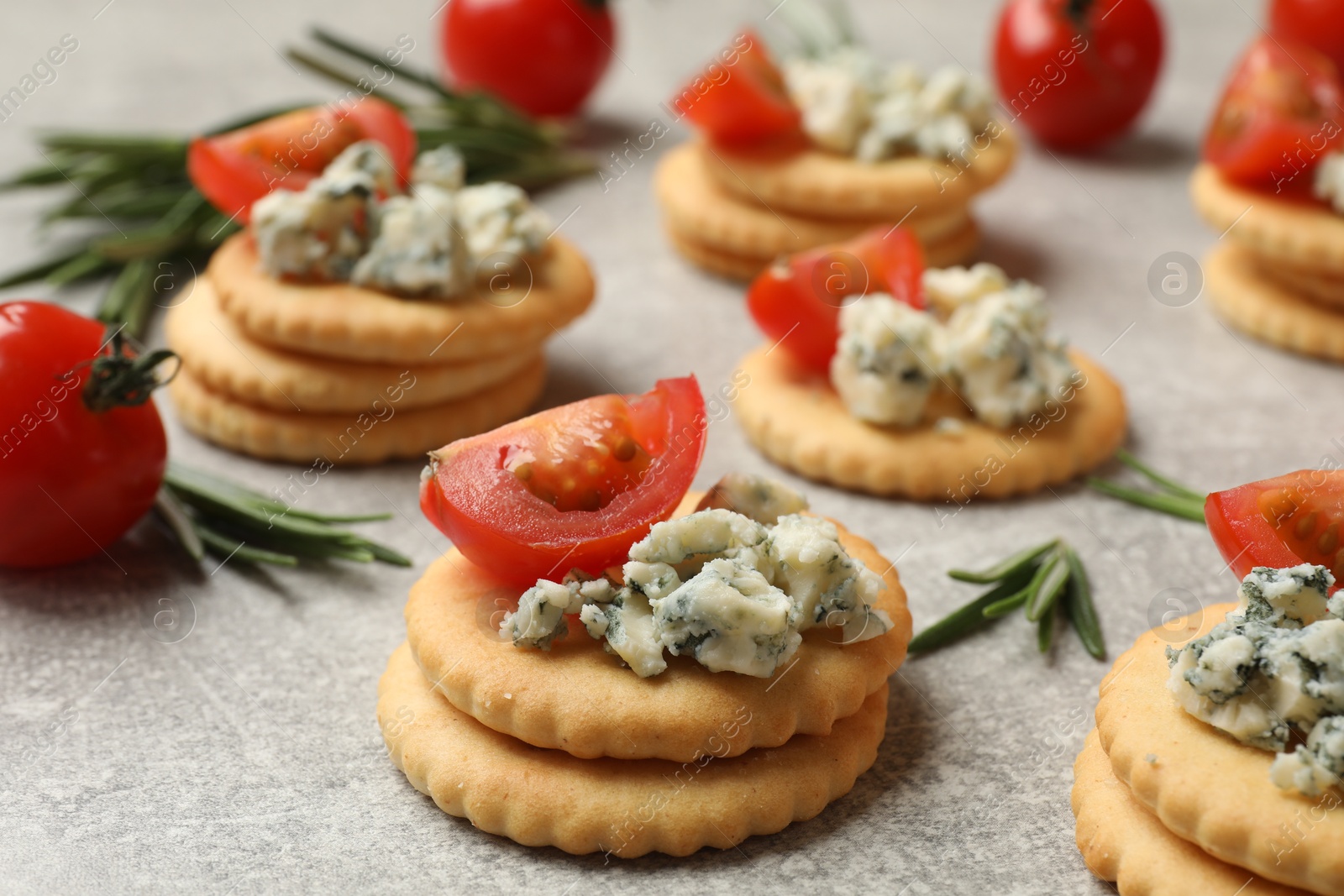 Photo of Tasty crackers with blue cheese, rosemary and tomatoes on grey textured table, closeup
