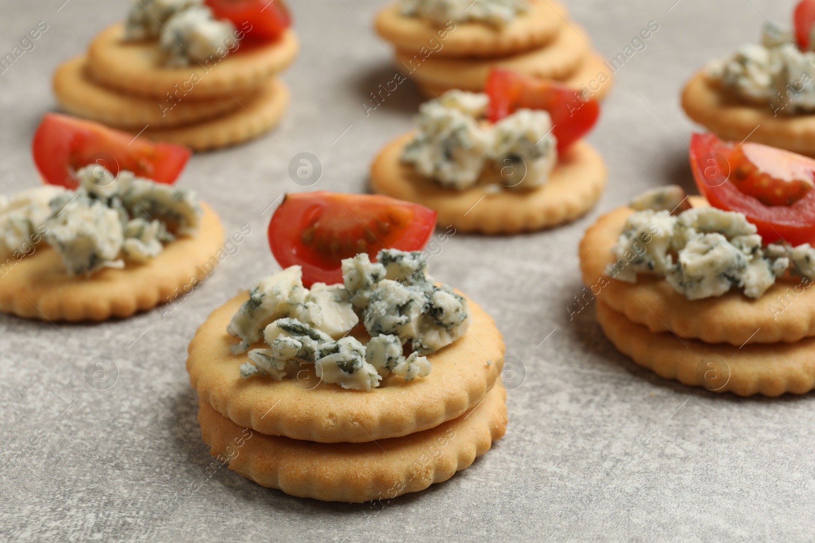 Tasty crackers with blue cheese and tomatoes on grey textured table, closeup Photo of Tasty crackers with blue cheese and tomatoes on grey textured table, closeup