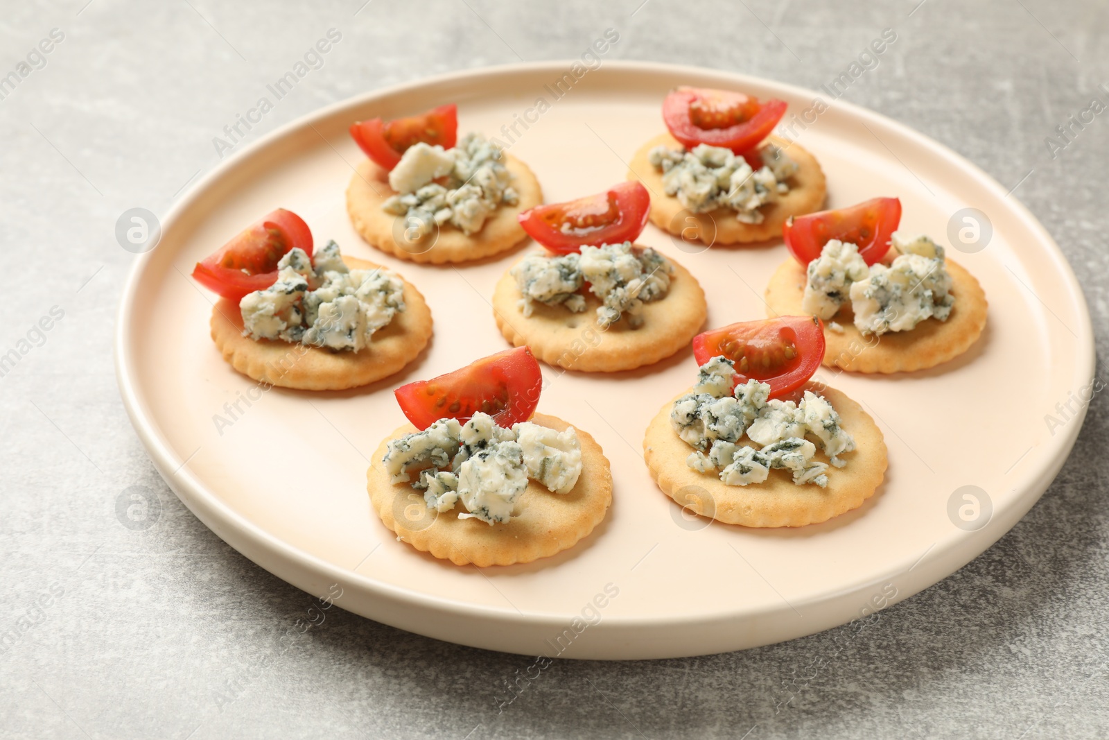 Tasty crackers with blue cheese and tomatoes on grey textured table, closeup Photo of Tasty crackers with blue cheese and tomatoes on grey textured table, closeup
