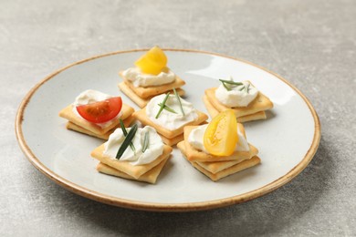 Photo of Tasty crackers with cream cheese, rosemary and tomatoes on grey textured table, closeup