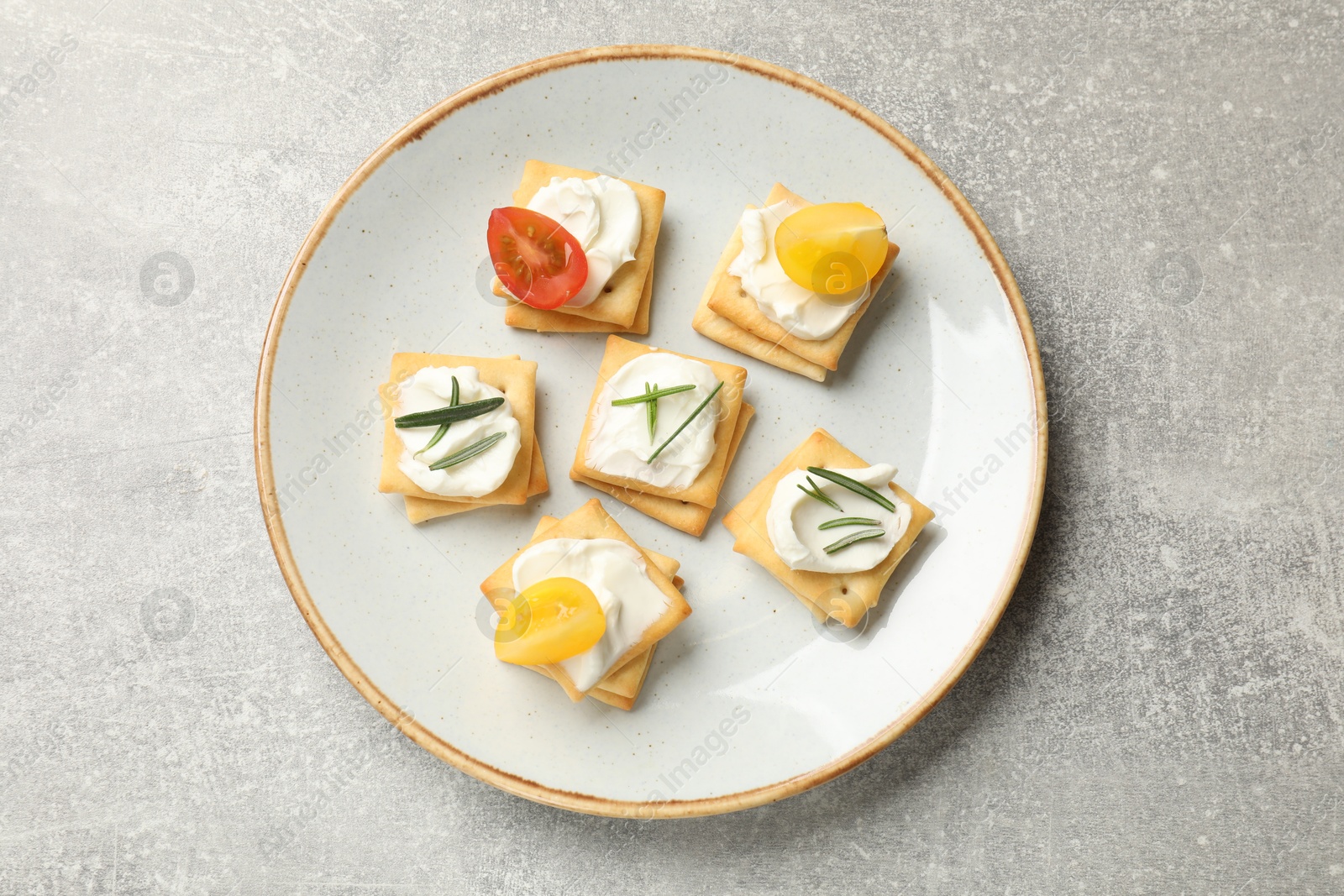 Tasty crackers with cream cheese, rosemary and tomatoes on grey textured table, top view Photo of Tasty crackers with cream cheese, rosemary and tomatoes on grey textured table, top view
