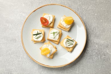 Photo of Tasty crackers with cream cheese, rosemary and tomatoes on grey textured table, top view