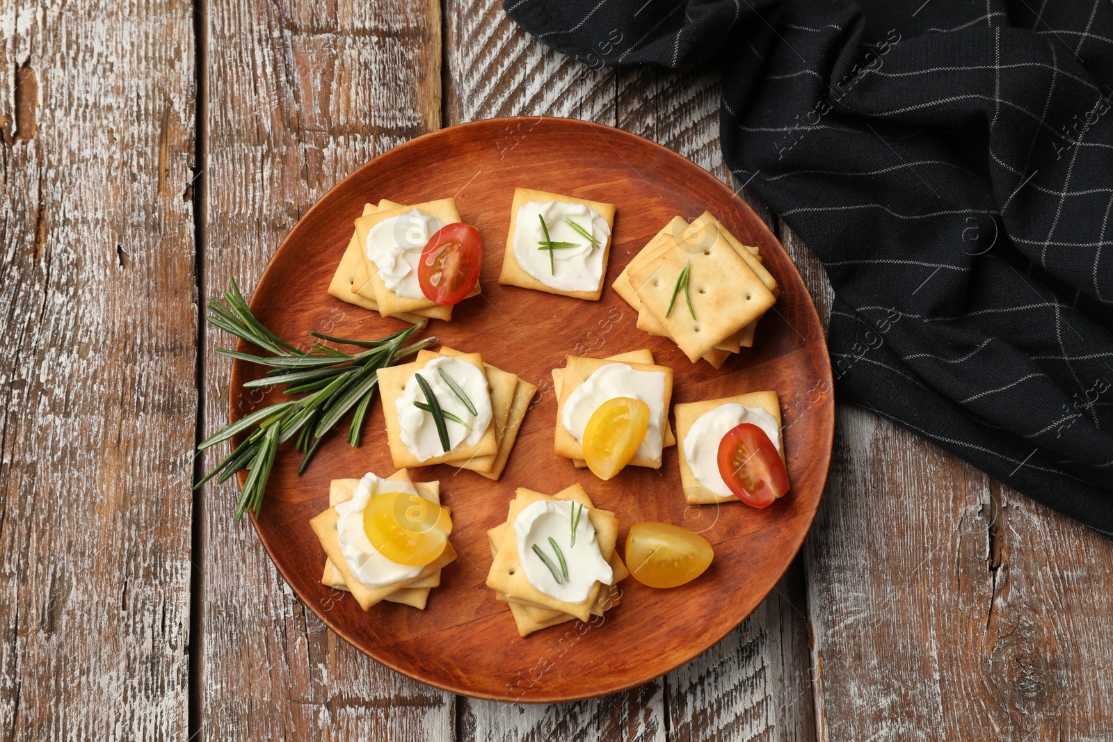 Tasty crackers with cream cheese, rosemary and tomatoes on wooden table, top view Photo of Tasty crackers with cream cheese, rosemary and tomatoes on wooden table, top view