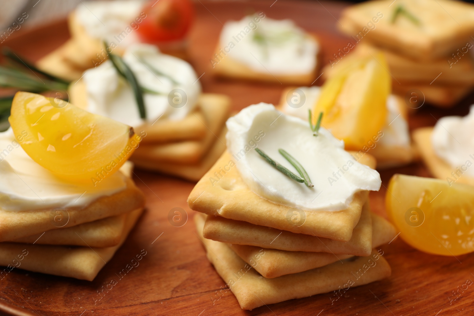Tasty crackers with cream cheese, rosemary and tomatoes on wooden plate, closeup Photo of Tasty crackers with cream cheese, rosemary and tomatoes on wooden plate, closeup