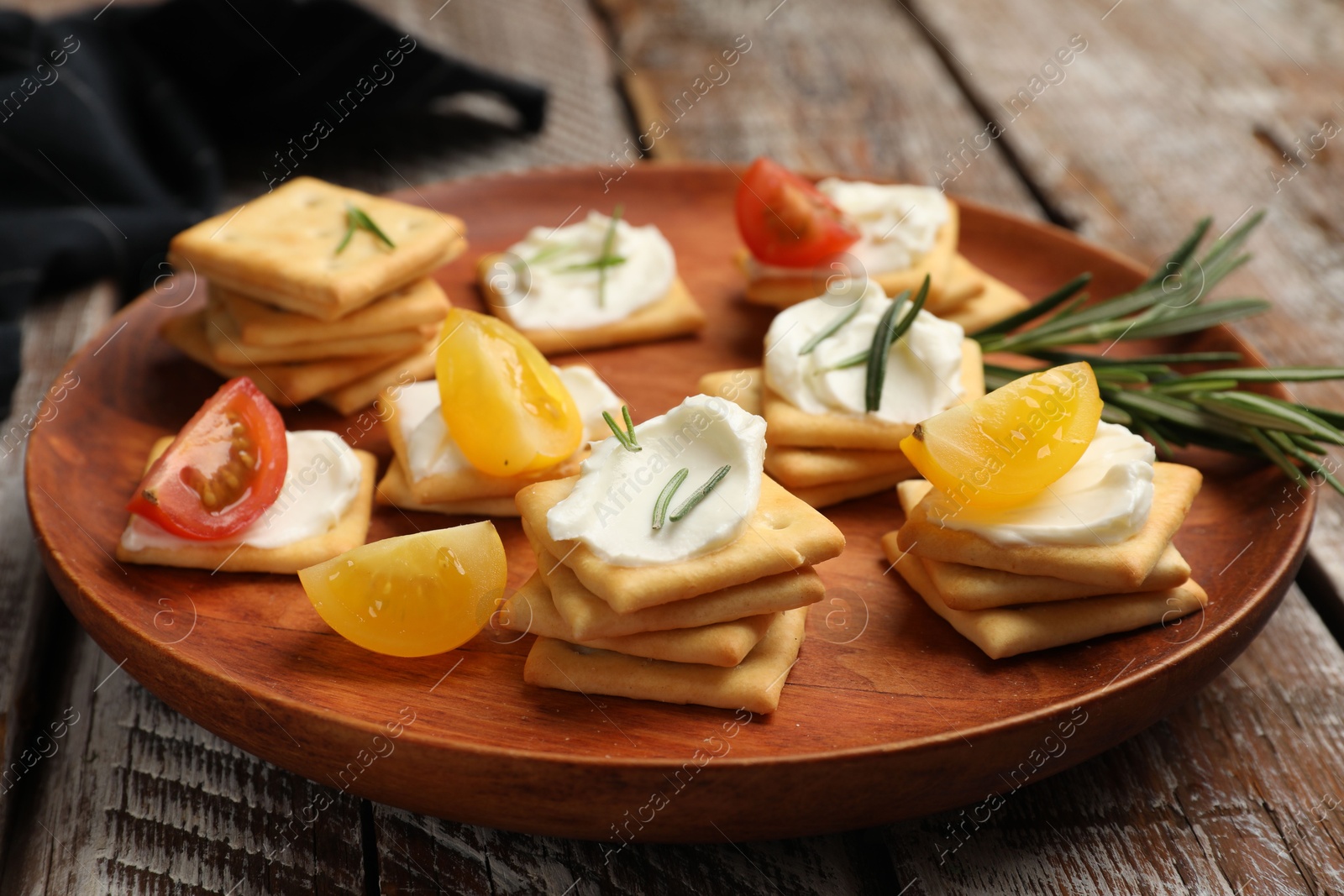Tasty crackers with cream cheese, rosemary and tomatoes on wooden table, closeup Photo of Tasty crackers with cream cheese, rosemary and tomatoes on wooden table, closeup