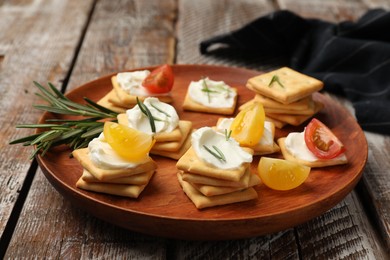 Photo of Tasty crackers with cream cheese, rosemary and tomatoes on wooden table, closeup