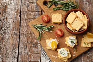 Photo of Tasty crackers with cream cheese, rosemary, salt and tomatoes on wooden table, top view. Space for text