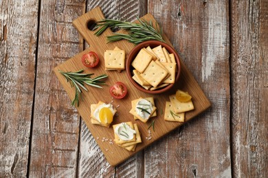 Photo of Tasty crackers with cream cheese, rosemary, salt and tomatoes on wooden table, top view