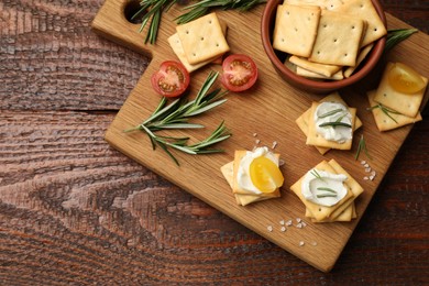 Photo of Tasty crackers with cream cheese, rosemary, salt and tomatoes on wooden table, top view