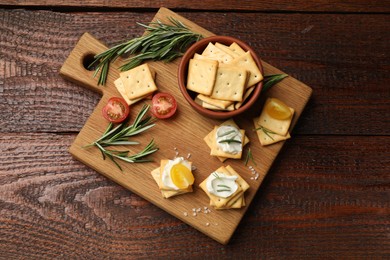 Photo of Tasty crackers with cream cheese, rosemary, salt and tomatoes on wooden table, top view