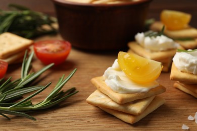 Photo of Tasty crackers with cream cheese, rosemary, salt and tomatoes on wooden table, closeup