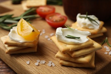 Photo of Tasty crackers with cream cheese, rosemary, salt and tomatoes on wooden table, closeup