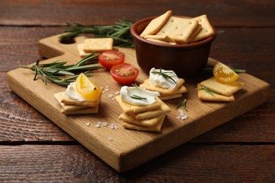 Photo of Tasty crackers with cream cheese, rosemary, salt and tomatoes on wooden table, closeup