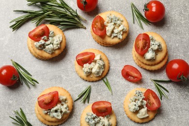 Photo of Tasty crackers with blue cheese, rosemary and tomatoes on grey textured table, flat lay