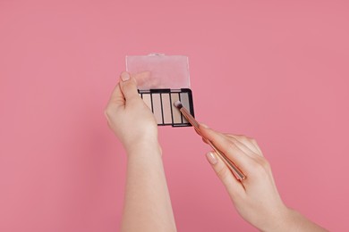 Photo of Woman with eyeshadow palette and brush on pink background, closeup