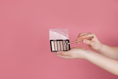 Photo of Woman with eyeshadow palette and brush on pink background, closeup. Space for text