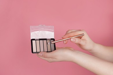 Photo of Woman with eyeshadow palette and brush on pink background, closeup
