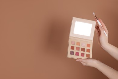 Photo of Woman with eyeshadow palette and brush on beige background, closeup. Space for text