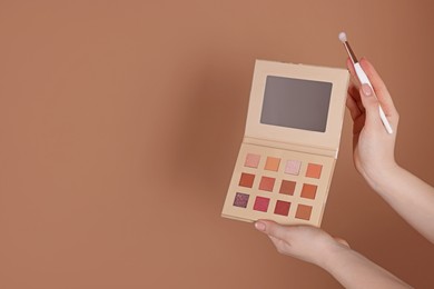 Photo of Woman with eyeshadow palette and brush on beige background, closeup. Space for text