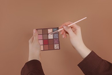 Photo of Woman with eyeshadow palette and brush on beige background, closeup