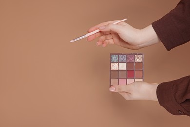 Photo of Woman with eyeshadow palette and brush on beige background, closeup. Space for text
