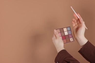 Photo of Woman with eyeshadow palette and brush on beige background, closeup. Space for text