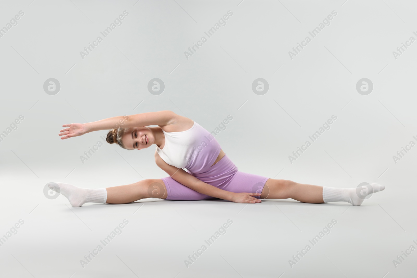 Girl in stylish clothes practicing split on light grey background. Dance Photo of Girl in stylish clothes practicing split on light grey background. Dance