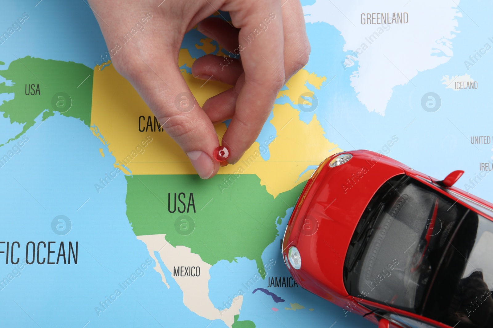 Road trip concept. Woman attaching pin to world map near car model, top view Photo of Road trip concept. Woman attaching pin to world map near car model, top view